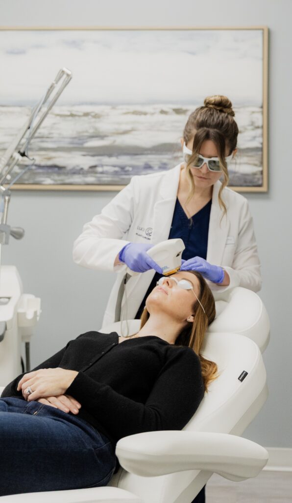 Juleit Coffey, PA-C, performing BBL Laser treatment on a patient in a dark navy shirt, laying on her back.